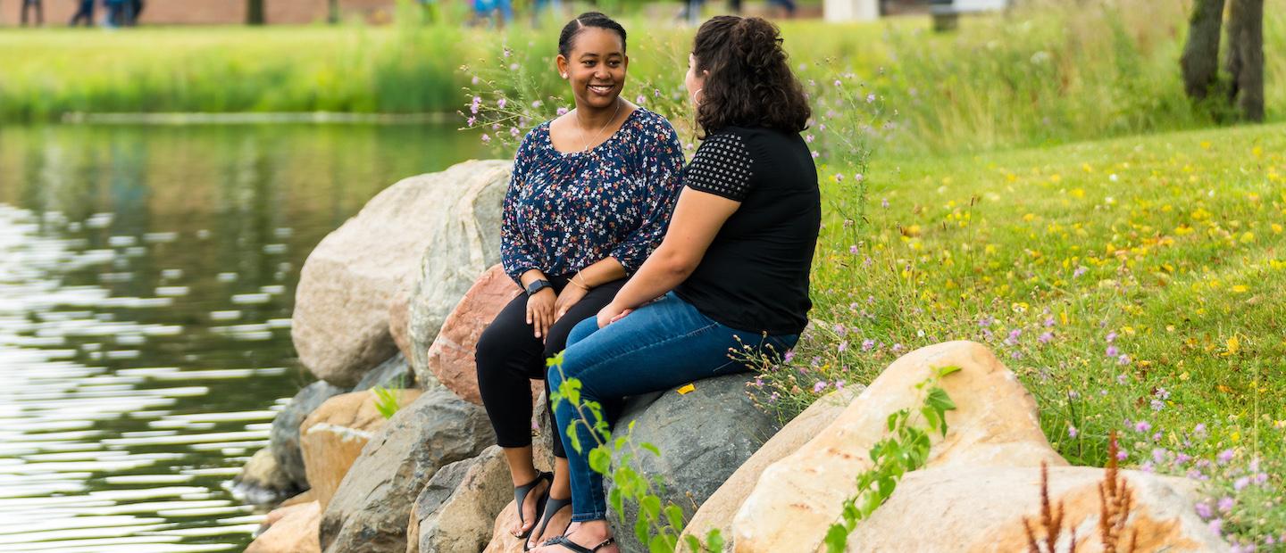两个女人坐在十大菠菜台子池塘边的岩石上.